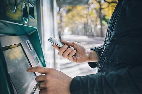 Eingabe in Geldautomaten mit Handy in der Hand