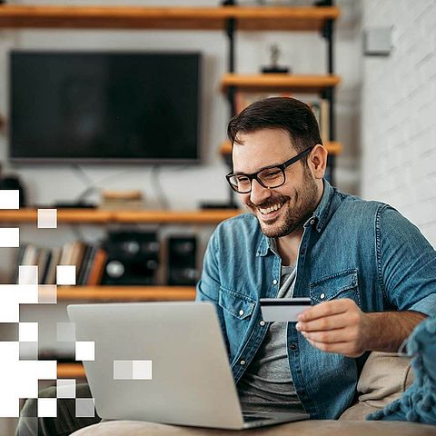 Mann sitzt lächelnd am Laptop mit Karte in der Hand